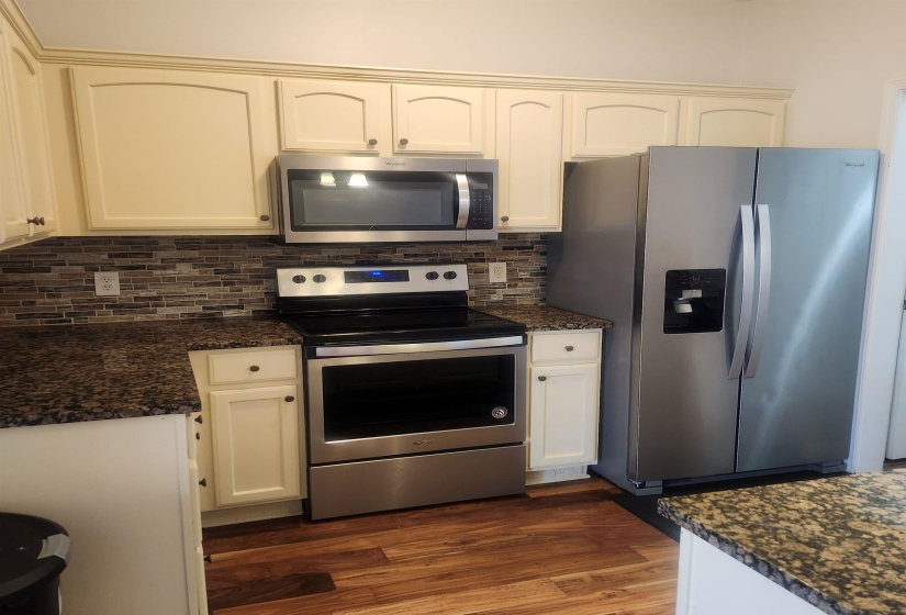 Kitchen featuring stainless steel appliances, dark wood-style flooring, dark stone counters, decorative backsplash, and white cabinets