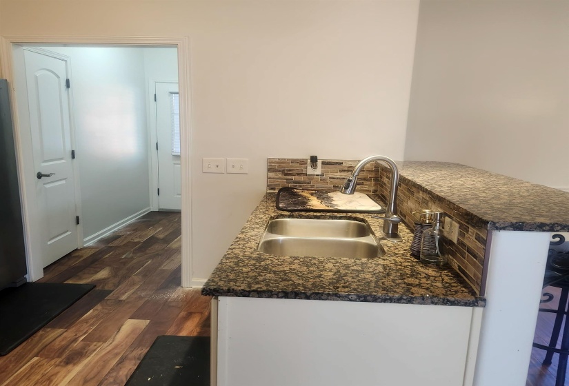 Kitchen featuring dark wood-type flooring, a peninsula, dark stone countertops, and backsplash