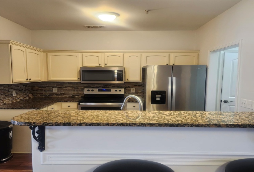 Kitchen featuring stainless steel appliances, tasteful backsplash, cream cabinets, and dark stone countertops