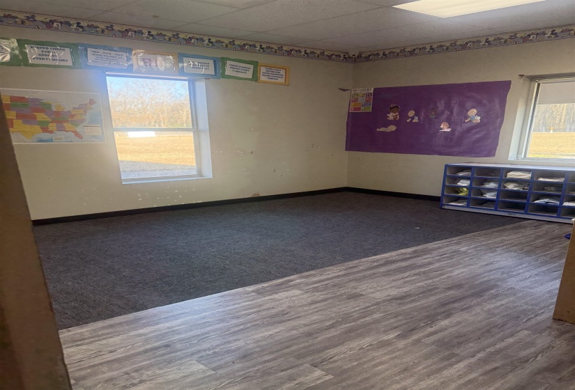 Empty room with dark colored carpet, a paneled ceiling, and dark wood-style flooring