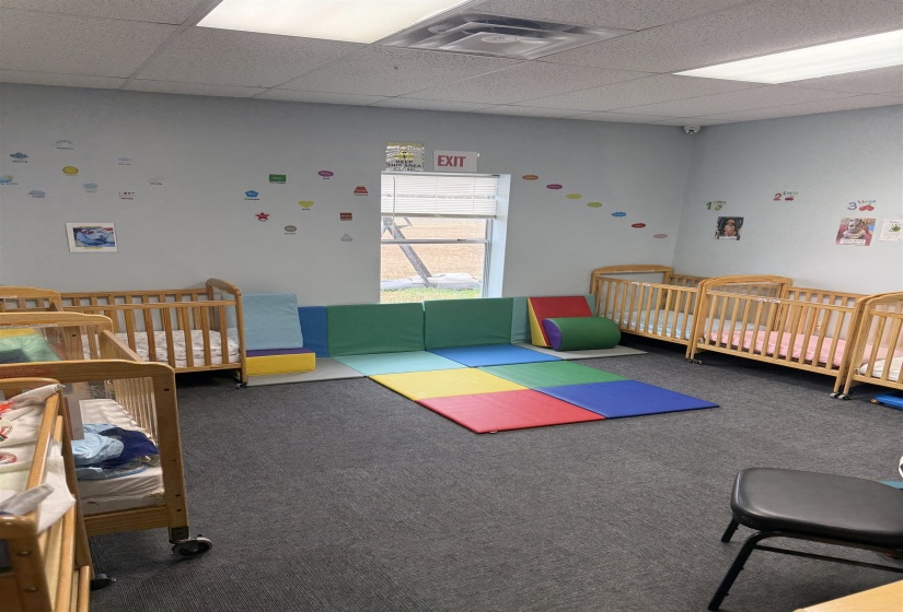 Carpeted bedroom featuring a nursery area and a drop ceiling