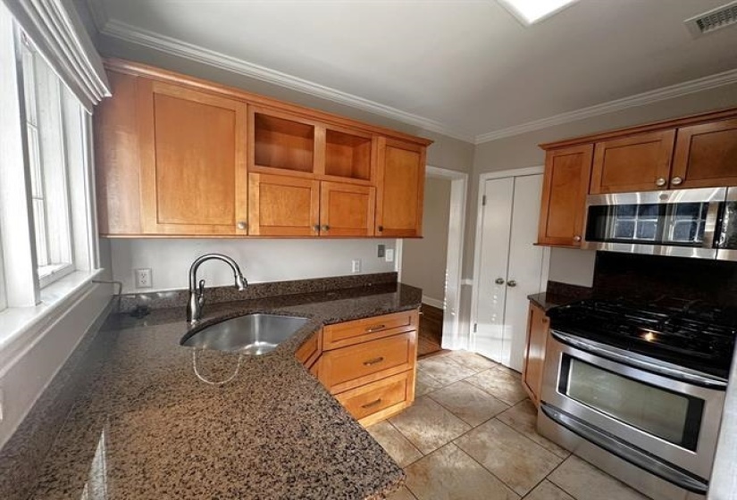 Kitchen with appliances with stainless steel finishes, crown molding, dark stone counters, brown cabinets, and open shelves