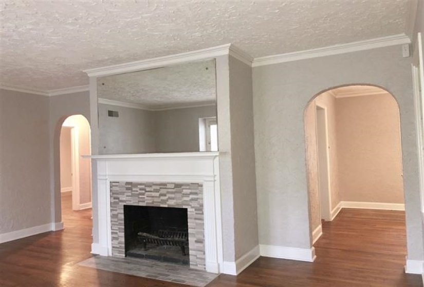 Unfurnished living room with arched walkways, dark wood-style floors, ornamental molding, a tile fireplace, and a textured ceiling