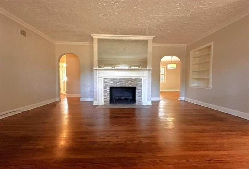 Unfurnished living room featuring arched walkways, built in shelves, dark wood-style floors, a textured ceiling, and crown molding