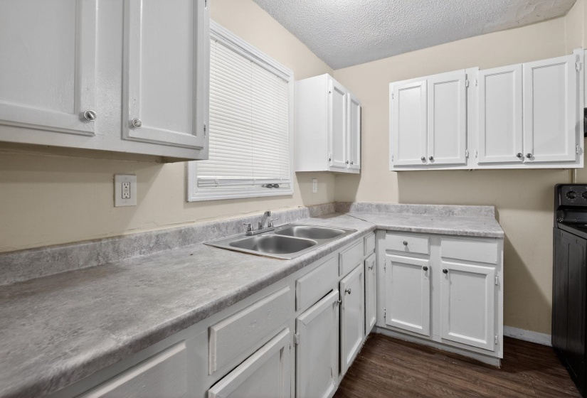 Kitchen with white cabinets, a textured ceiling, light countertops, black range, and dark wood-type flooring