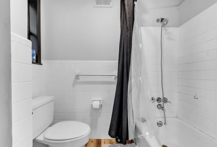 Full bath featuring visible vents, tile walls, a wainscoted wall, toilet, and shower / bathtub combination with curtain