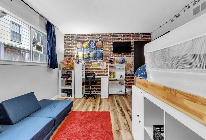 Interior space featuring an accent wall, visible vents, brick wall, and wood finished floors
