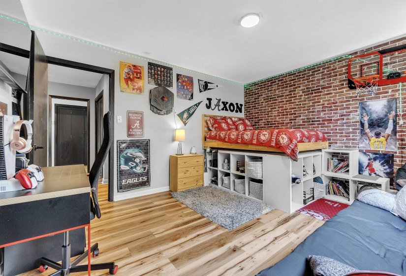 Bedroom with baseboards, brick wall, and wood finished floors