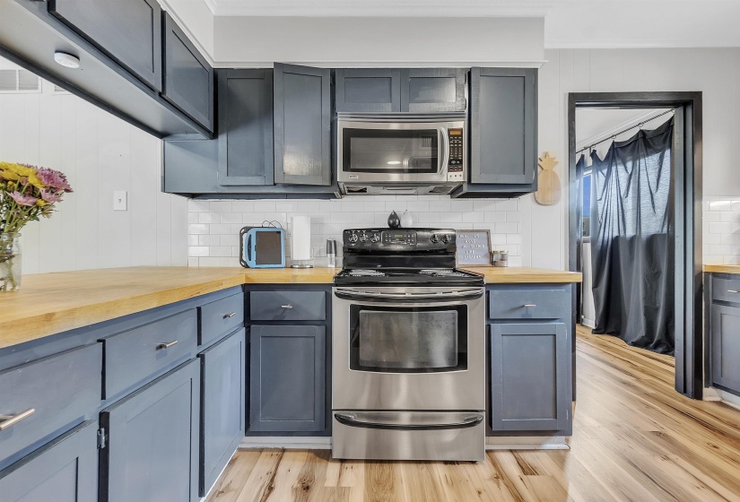Kitchen with crown molding, butcher block countertops, light wood-style flooring, backsplash, and stainless steel appliances