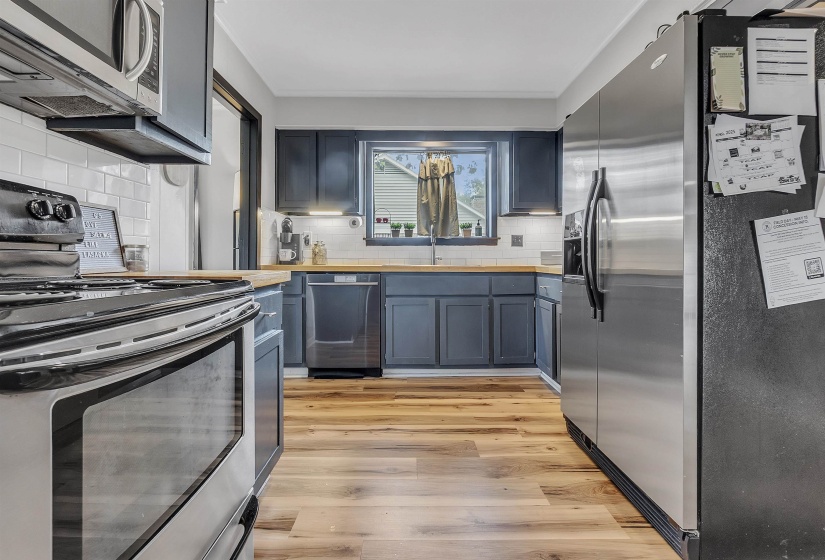 Kitchen with light wood-style floors, tasteful backsplash, stainless steel appliances, and butcher block countertops