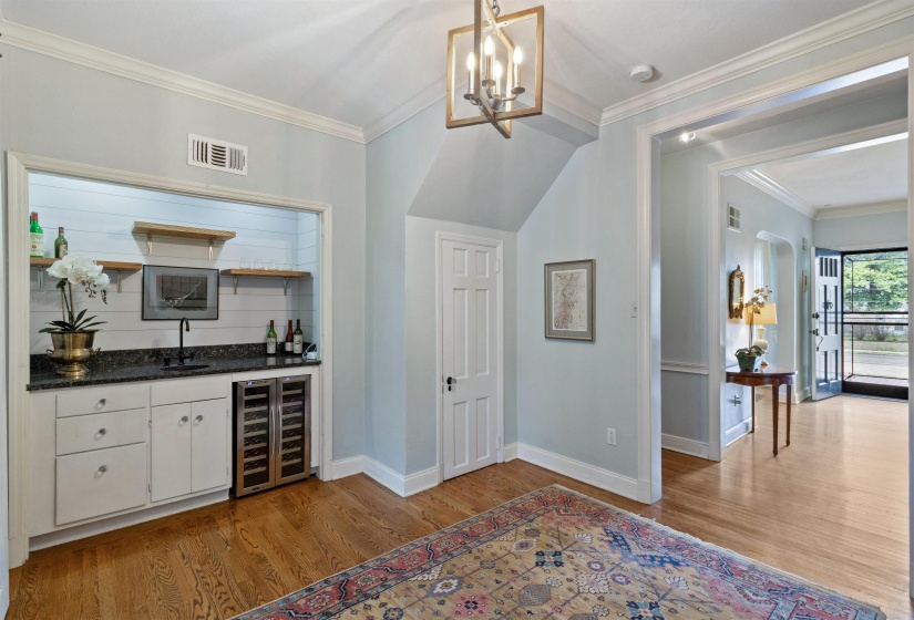 Indoor wet bar featuring wine cooler, ornamental molding, open shelves, dark stone countertops, and light wood finished floors