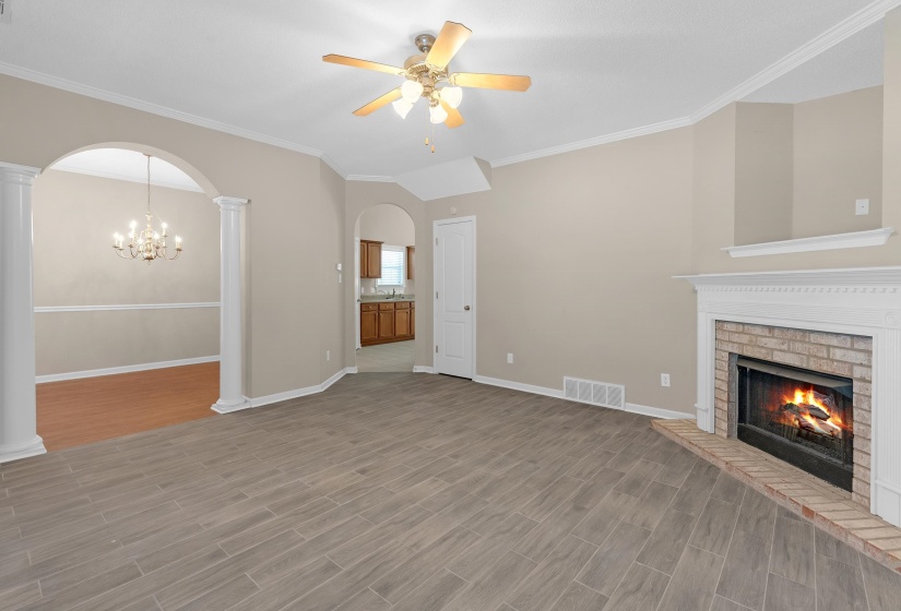 Unfurnished living room with wood finish floors, crown molding, arched walkways, a fireplace, and a chandelier