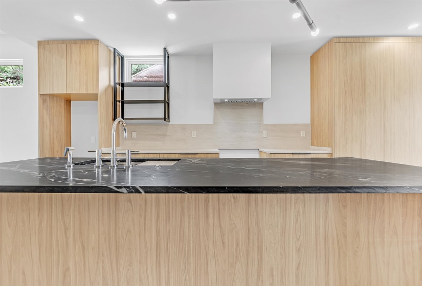 Kitchen with modern cabinets, light brown cabinetry, premium range hood, dark stone countertops, and healthy amount of natural light