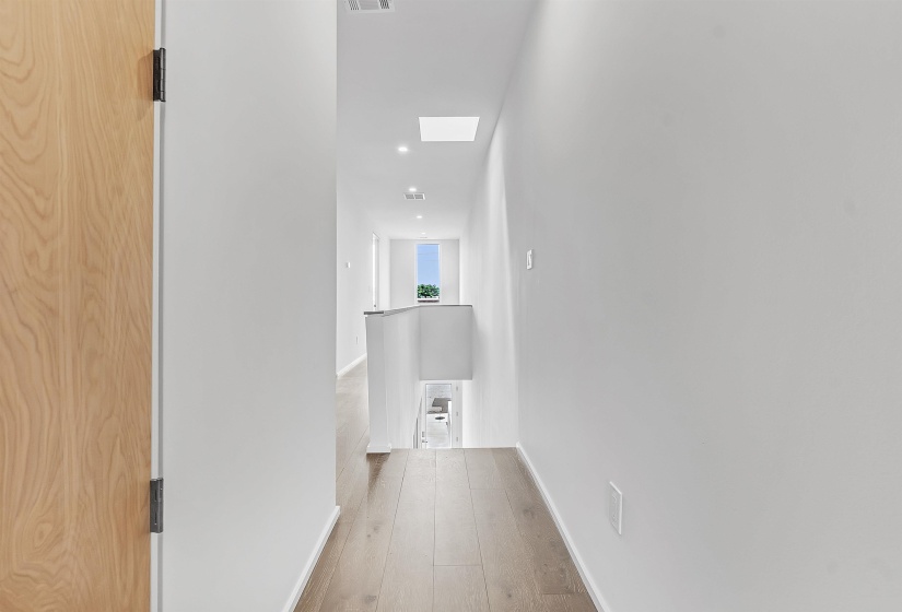 Hallway with wood-type flooring, an upstairs landing, baseboards, recessed lighting, and a skylight