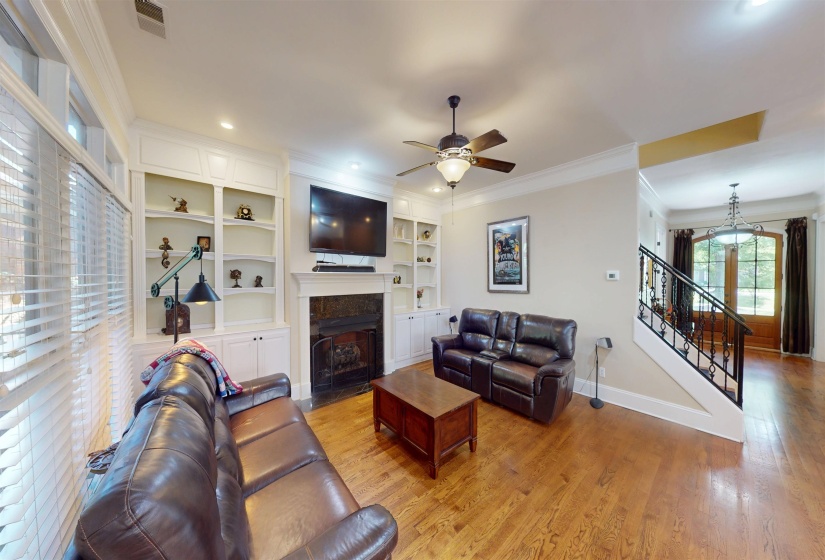 Living area featuring ornamental molding, light wood-style flooring, a fireplace with flush hearth, ceiling fan, and stairway