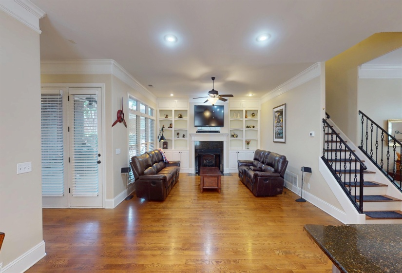 Living room featuring stairway, crown molding, a fireplace, built in shelves, and light wood finished floors