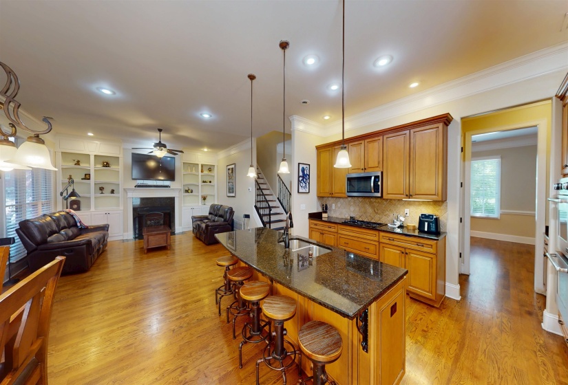 Kitchen with dark stone counters, open floor plan, crown molding, brown cabinetry, and light wood finished floors