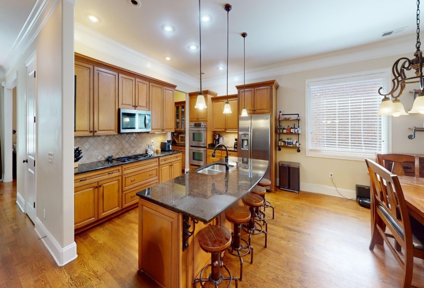 Kitchen with crown molding, dark stone countertops, brown cabinets, a breakfast bar area, and an island with sink