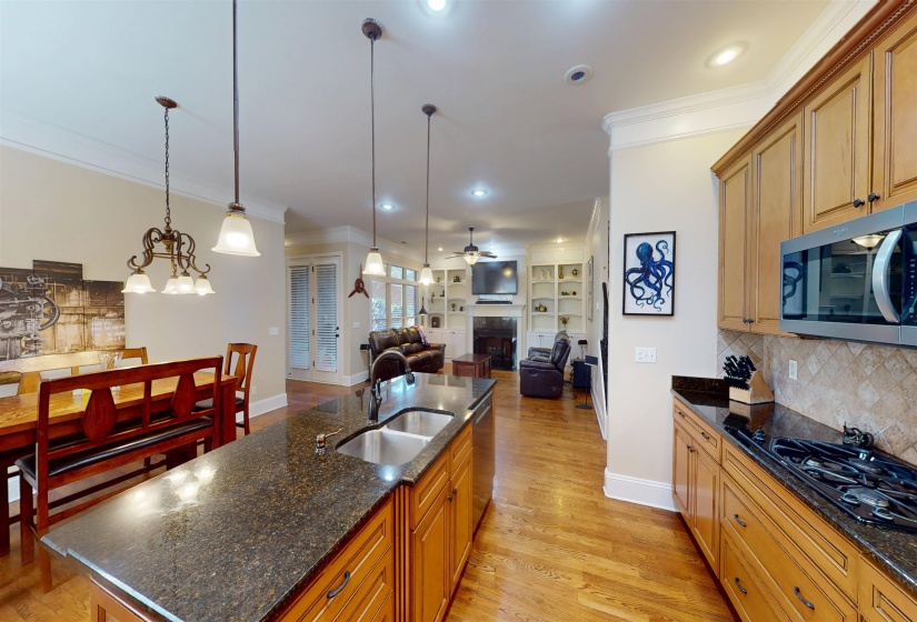 Kitchen with ornamental molding, a fireplace, light wood finished floors, a kitchen island with sink, and open floor plan