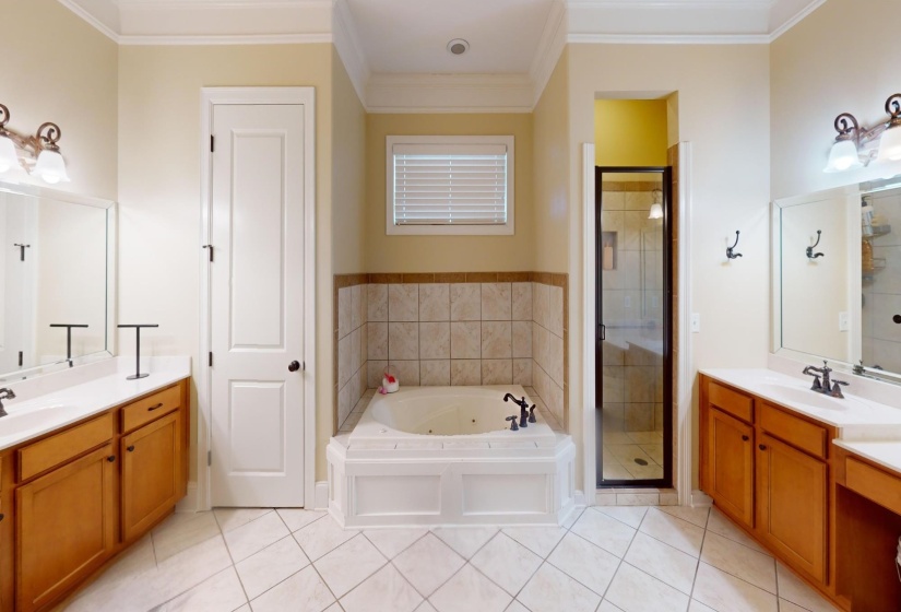 Full Ensuite bathroom with a whirlpool tub, a stall shower, light tile patterned floors, two vanities, and ornamental molding