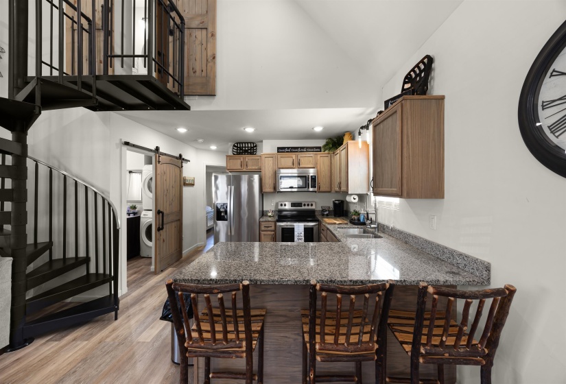 Kitchen featuring stainless steel appliances, a barn door, light wood finished floors, stone countertops, and a peninsula