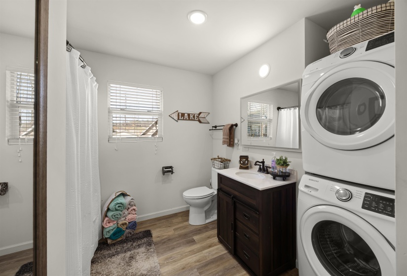 Washroom featuring stacked washer and dryer, a sink, laundry area, baseboards, and light wood-style floors