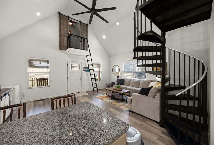 Living room featuring high vaulted ceiling, baseboards, ceiling fan, wood finished floors, and stairway