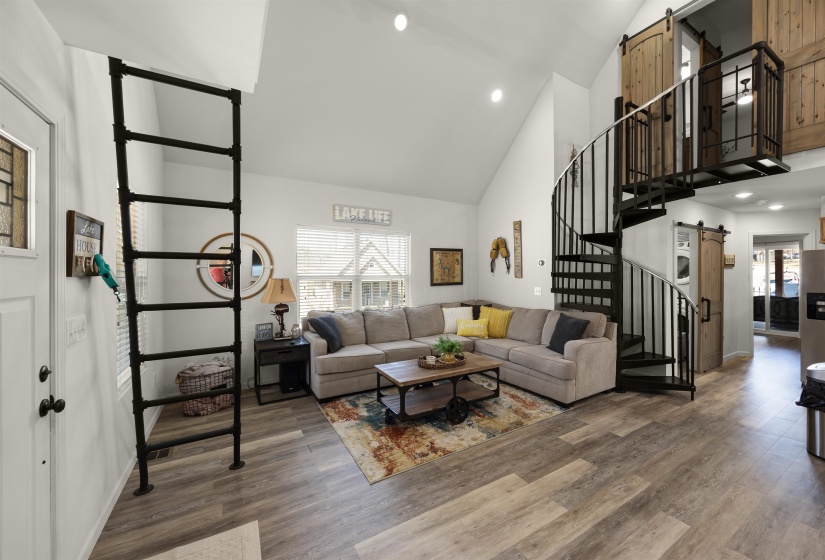 Living room with stairs, high vaulted ceiling, a barn door, and wood finished floors