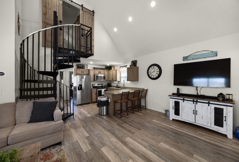 Living room with stairs, high vaulted ceiling, baseboards, a barn door, and wood finished floors