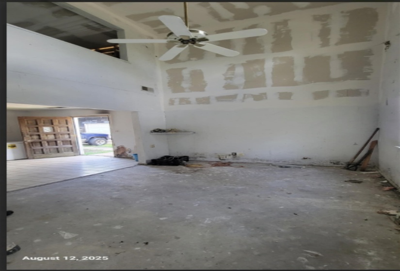 Empty room with a high ceiling, unfinished concrete flooring, and ceiling fan
