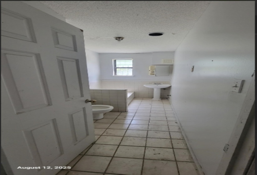 Full bath featuring tile walls, light tile patterned floors, a textured ceiling, a wainscoted wall, and a garden tub