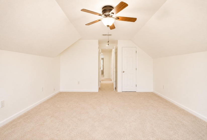 Spacious room featuring neutral carpeting, white walls, and an angled ceiling line