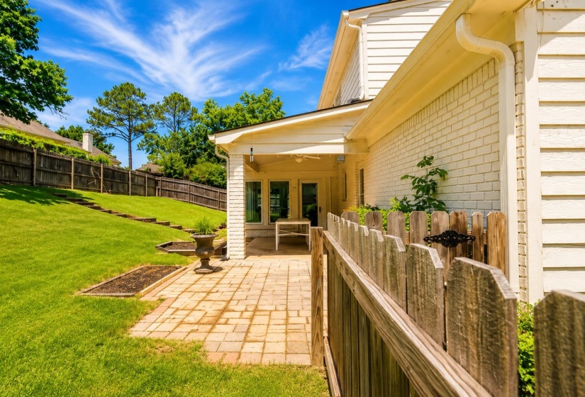 Expansive sloped backyard featuring mature trees, a wood privacy fence, and a brick paver patio