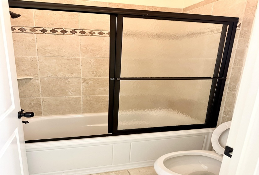 Bathroom with enclosed tub / shower combo, tile patterned flooring, and toilet