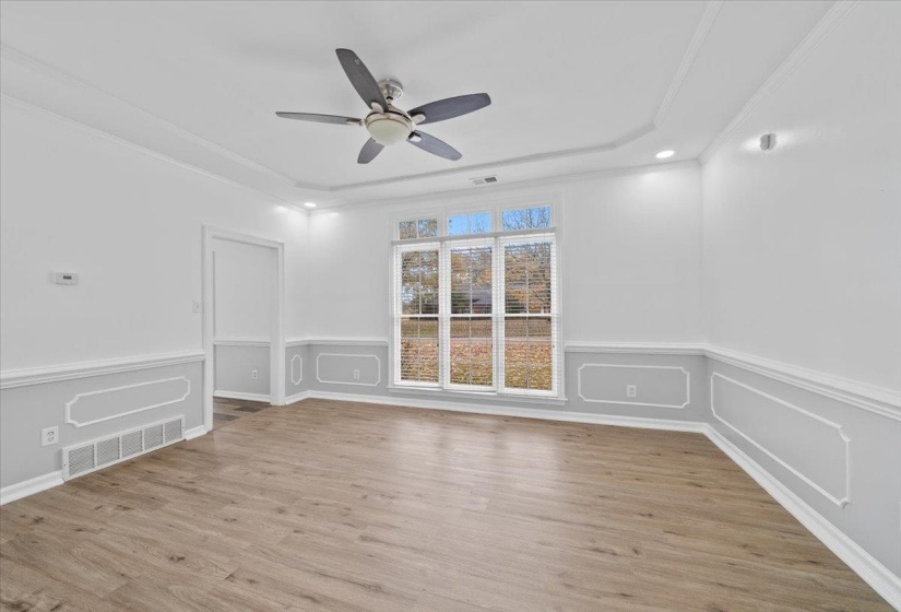 Spare room featuring ornamental molding, light wood-type flooring, a tray ceiling, wainscoting, and ceiling fan