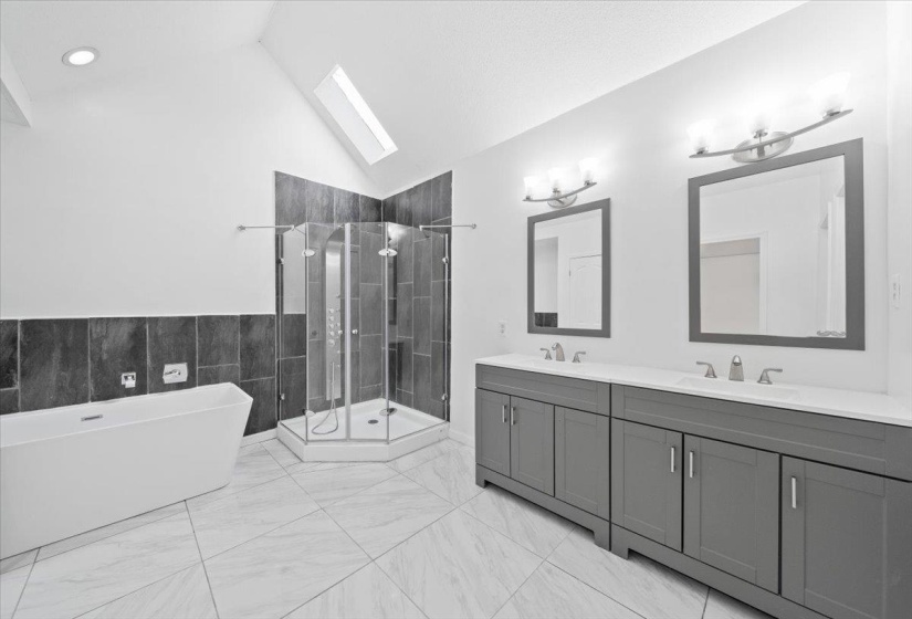 Full bathroom featuring a skylight, a soaking tub, a shower stall, double vanity, and vaulted ceiling