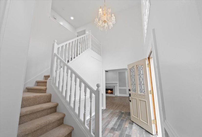 Entrance foyer featuring a lit fireplace, wood finished floors, stairs, a chandelier, and a towering ceiling