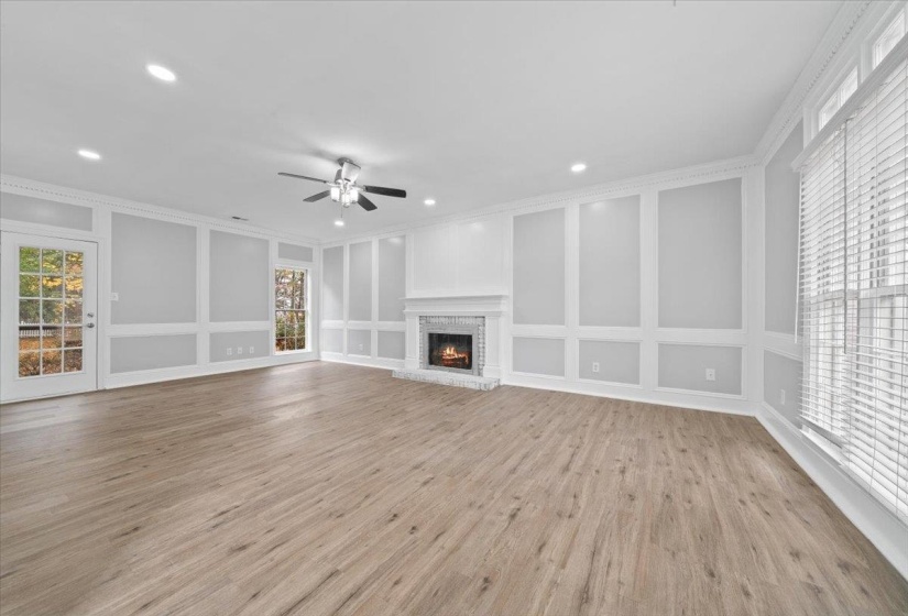 Unfurnished living room with a decorative wall, a brick fireplace, light wood-type flooring, crown molding, and recessed lighting