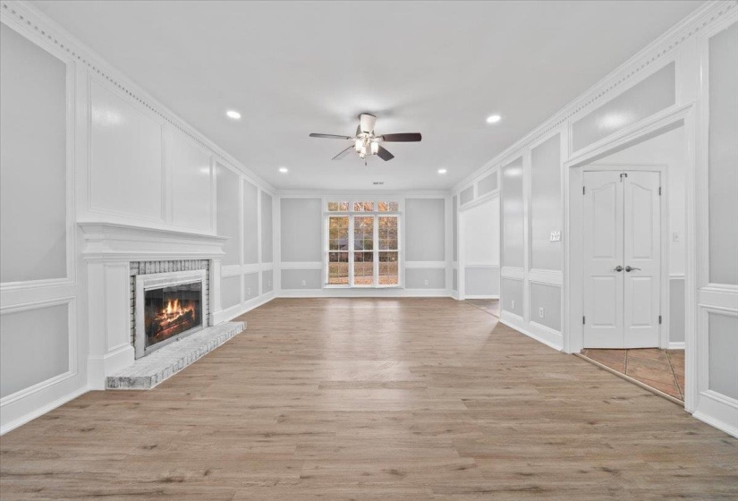 Unfurnished living room with light wood-style flooring, a brick fireplace, a decorative wall, crown molding, and a ceiling fan
