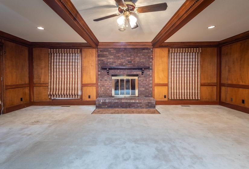 Unfurnished living room with beam ceiling, wood walls, a brick fireplace, a ceiling fan, and a decorative wall