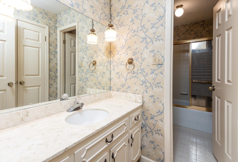 Bathroom featuring wallpapered walls, enclosed tub / shower combo, vanity, and a textured ceiling