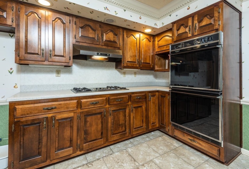 Kitchen with light countertops, brown cabinets, under cabinet range hood, stone tile flooring, and stainless steel gas cooktop