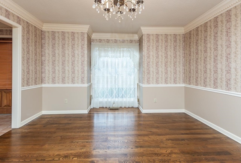 Spare room with wallpapered walls, a chandelier, ornamental molding, dark wood finished floors, and wainscoting