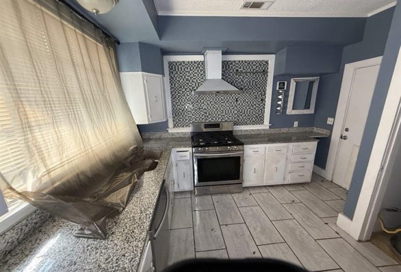 Kitchen with white cabinets, stainless steel range with gas stovetop, dark stone counters, wood finish floors, and decorative backsplash
