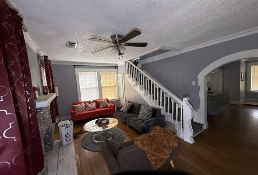 Living room with crown molding, a tiled fireplace, arched walkways, wood finished floors, and a textured ceiling