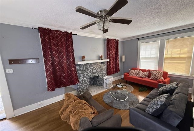 Living area featuring wood finished floors, ceiling fan, a textured ceiling, a tile fireplace, and crown molding