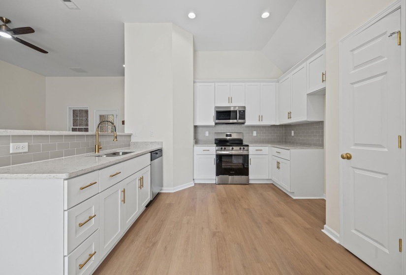 Kitchen featuring appliances with stainless steel finishes, white cabinets, tasteful backsplash, vaulted ceiling, and light stone countertops