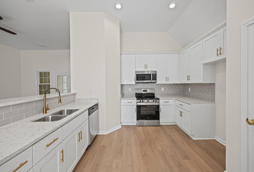 Kitchen featuring stainless steel appliances, tasteful backsplash, light stone countertops, white cabinetry, and lofted ceiling
