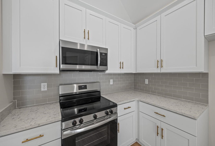 Kitchen featuring stainless steel appliances, white cabinetry, light stone counters, backsplash, and vaulted ceiling