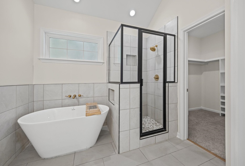 Full bathroom featuring a stall shower, a soaking tub, a spacious closet, light tile patterned floors, and tile walls